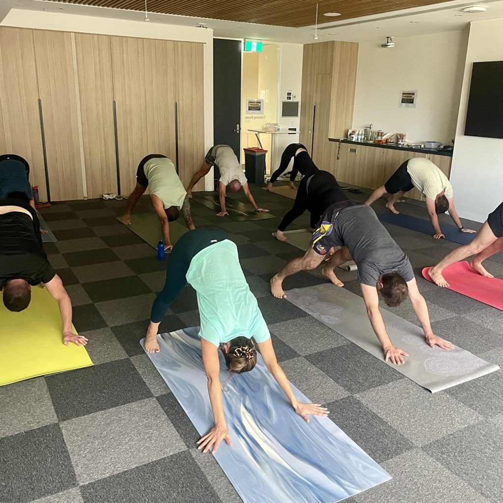 Employees of a corporation participating in a corporate yoga program doing downward facing dog in a meeting room